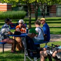 Group of four people sitting around a table, two men sitting in lawn chairs
